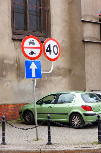 A vertical shot of a Peugeot car parked by a building in Poznan, Poland with road signs next to it