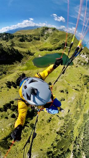 An overhead shot of a person paragliding over the Alps mountains with mountains and lake in the background