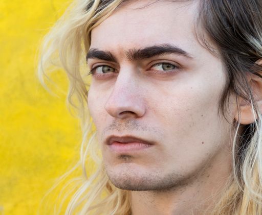 Blond attractive male model with long hair looking at the camera with yellow background