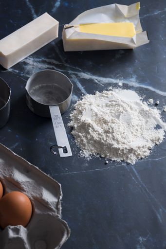 A close-up of baking ingredients including flour, butter, and eggs on a dark marble countertop
