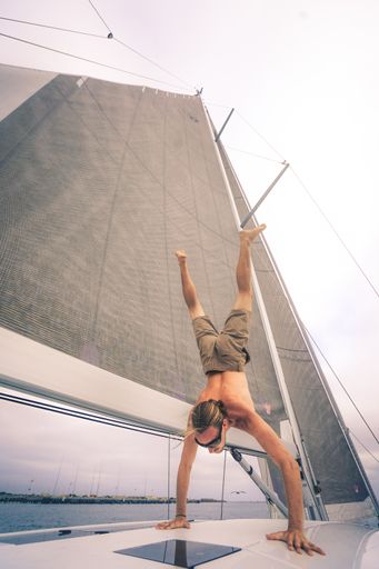 A vertical shot of a young male doing acrobatics and walking on hands on the ship during daytime