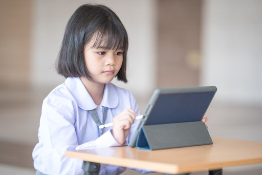 A Southeast Asian school girl in a uniform with short black hair drawing on a tablet with a pe