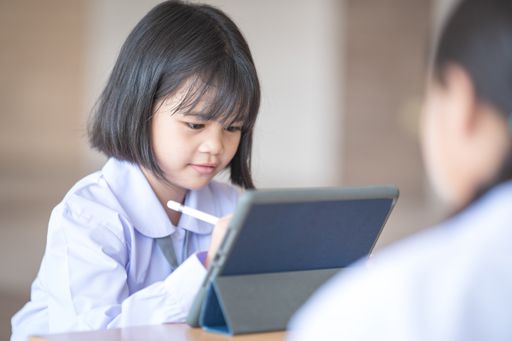 A Southeast Asian school girl in a uniform with short black hair drawing on a tablet with a pen