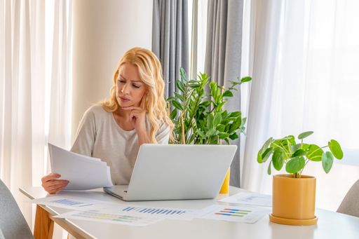 A young beautiful Serbian woman looking at her notes while working on the laptop in her room