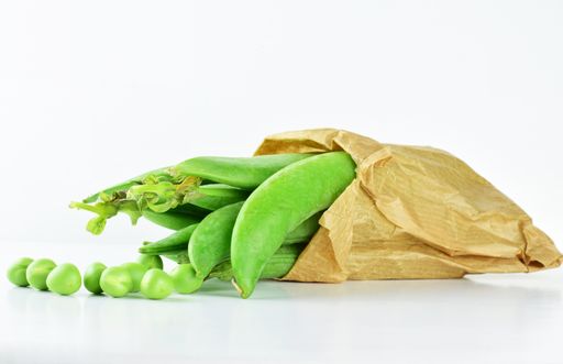 A closeup shot of garden peas in a kraft paper bag isolated on white background.