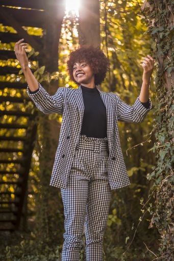 An attractive young female with afro hair in a formal outfit happily dancing in a park in Spain