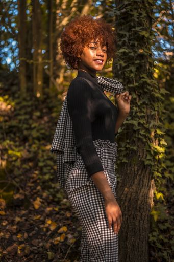 A portrait of an attractive young female with afro hair in a formal outfit holding her coat in a park in Spain