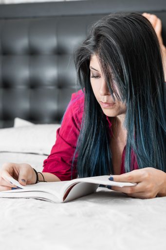 A portrait of a Hispanic female reading a book in the bed
