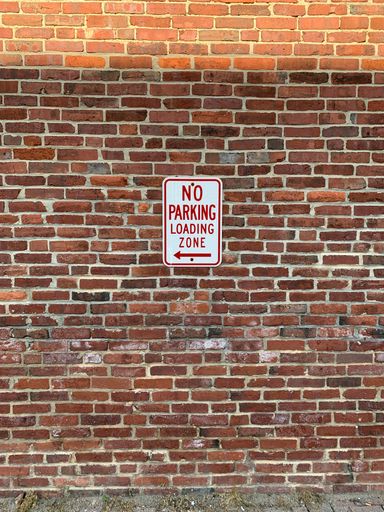 A vertical shot of a brick wall with No parking sign under the sunlight