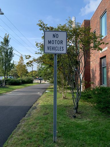 A vertical shot of a sign pole with No motor vehicles notes near the path next to the brick building