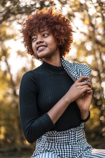 A portrait of an attractive young female with afro hair in a formal outfit holding her coat in a park in Spain