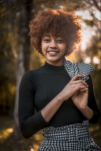 A portrait of an attractive young female with afro hair in a formal outfit holding her coat in a park in Spain