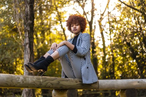 A beautiful young female with afro hair in a formal outfit sitting on a tree log in a park in Spain