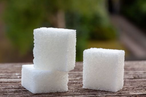 A closeup of small square sugar cubes on a wooden table outdoors with a blurry background