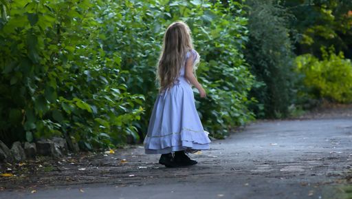A rear view of a little girl in a white dress standing on the path near the trees