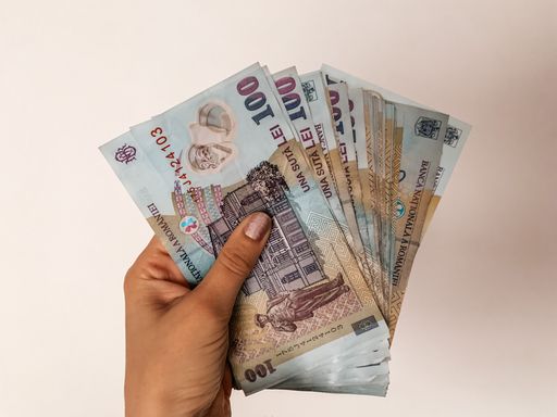 A closeup of a person holding cash Romanian leu against a beige background