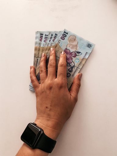 A closeup of a female hand holding Romanian money (100 LEI bills) on a pink surface