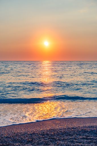 A vertical shot of a gorgeous bright sun shining down on a calm sea at Lefkada, Greece during sunset