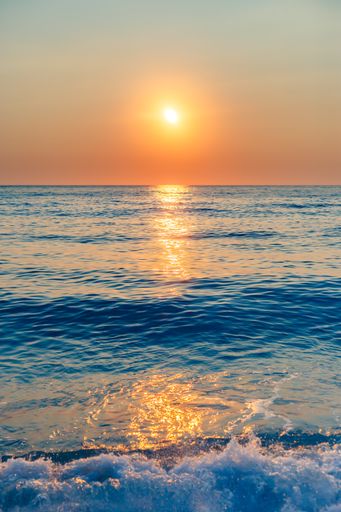 A beautiful vertical shot of a golden sun shining brightly down on the deep blue sea at Lefkada, Greece