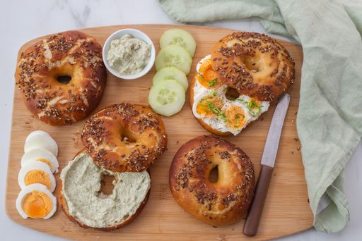 A top view of whole grain bagels with eggs, cucumber and cheese on a wooden board