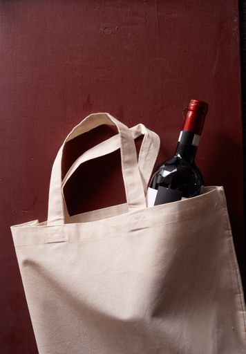 A vertical shot of a bottle of wine in an eco-friendly tote bag on a red background