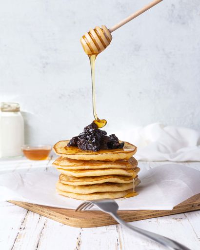 A closeup shot of a honey dipper on top of pancakes with berries