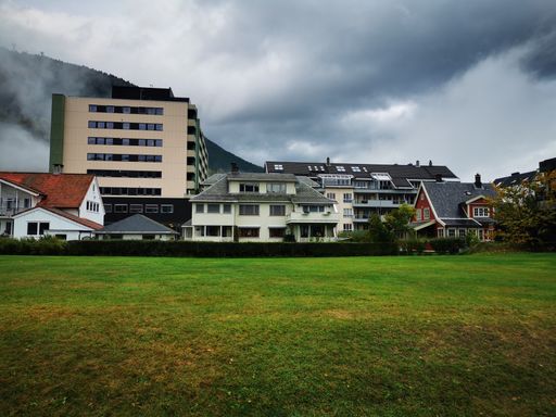 A small town foggy buildings with clean grass and mountain behind.