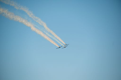 Three planes perform an aerial maneuver, leaving a trail of smoke against a clear blue sky.