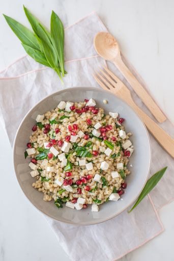 A top view of a barley salad and wooden utensils on a white napkin