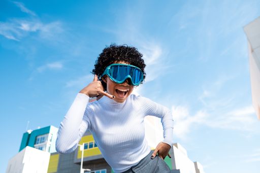 A cheerful young African American lady with curly hair wearing ski goggles in a residential area