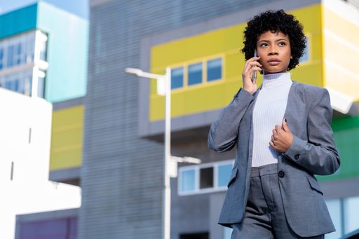 A cool young curly-haired African American lady dressed professionally talking on her phone outdoors