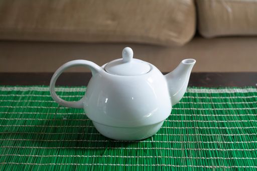 A closeup shot of a white teapot on a green tablecloth indoors
