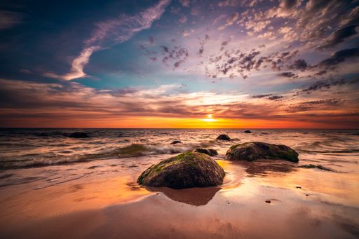 A group of small rock formations and a dramatic sunset sky over the tranquil Baltic Sea in Lithuania