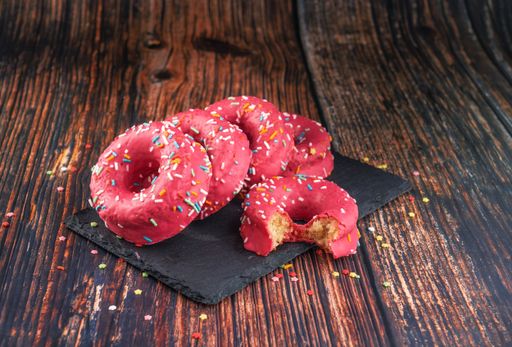 A stack of pink donuts decorated with colorful sprinkles on a black stone-plate