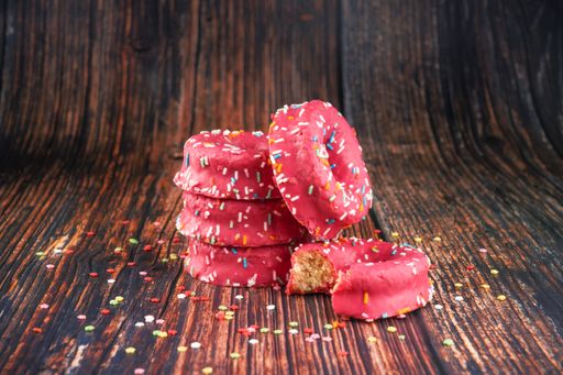 A stack of pink donuts decorated with colorful sprinkles on a wooden background