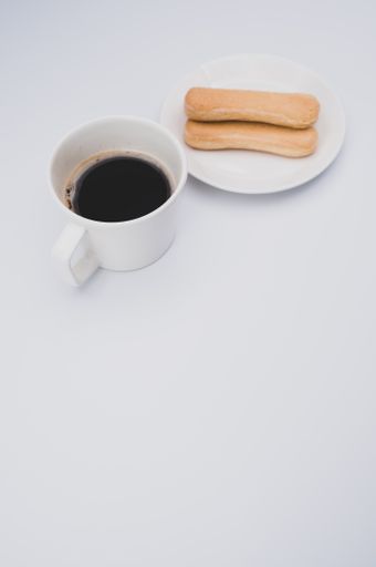 black coffee in a mug and plate with savoiardi biscuits on a wooden background with copy space