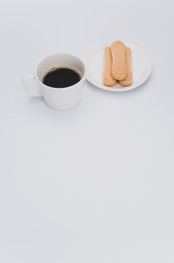 black coffee in a mug and plate with savoiardi biscuits on a wooden background with copy space
