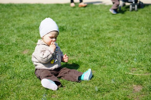 A closeup shot of a cute Caucasian baby boy sitting on the grass