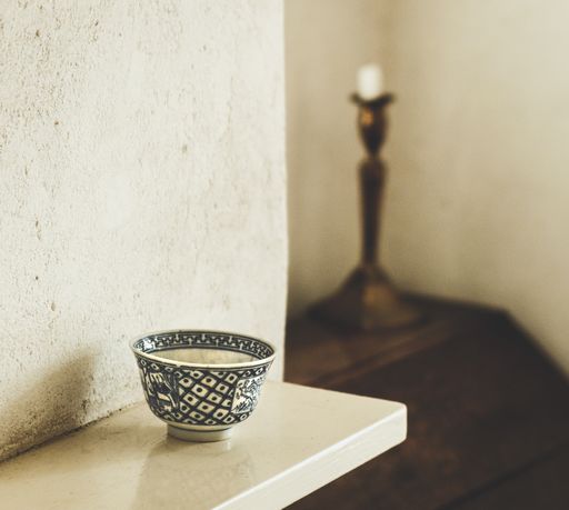 A bowl put on the shelf in front of the wall behind the candleholder