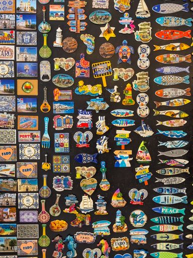 Assorted colorful magnets on display featuring iconic motifs from Faro, Algarve and Portugal, including tiles, fish, and local symbols.