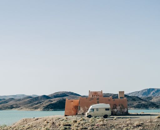 A wide angle shot of a car in front of a building surrounded by the lake and mountains
