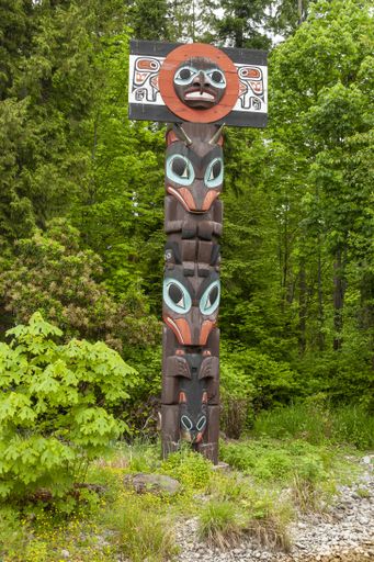 A vertical picture of a Totem Pole against greenery in Stanley Park, Canada