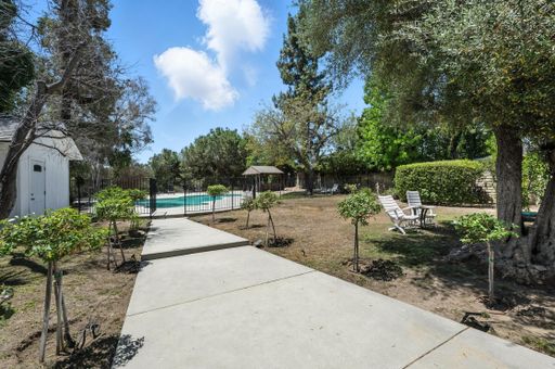 Charming single-level home featuring large pool, mature trees, mountain views, spacious interiors, and covered outdoor seating.