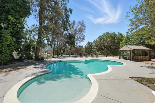 Charming single-level home featuring large pool, mature trees, mountain views, spacious interiors, and covered outdoor seating.