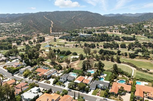 Overhead image of a wide suburban housing development, complete with green spaces, mature trees, and a golf course under open skies.