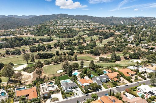 Top-down view of a peaceful suburb dotted with homes, vibrant foliage, and a golf course stretching out under a bright sky.
