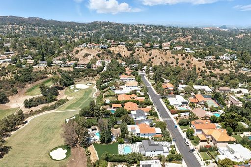 High-angle view of an extensive suburban neighborhood with well-kept homes, green trees, and a golf course beneath a clear blue sky.
