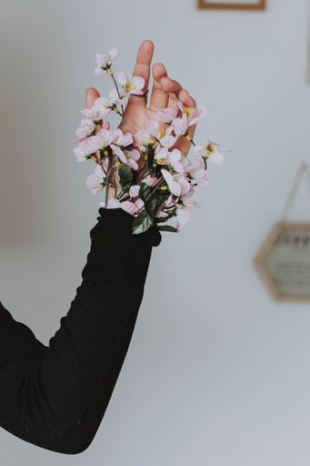 A vertical shot of a female's hand with a bouquet of flowers sticking out of her sleeve