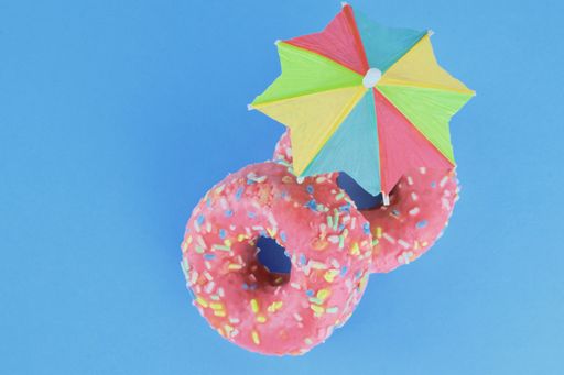 A closeup shot of two pink yummy donuts with a colorful umbrella  on a blue background