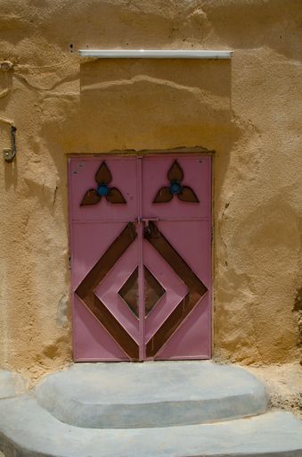 A vertical shot of a pink and brown ornate metal entrance door with a staircase in front of it